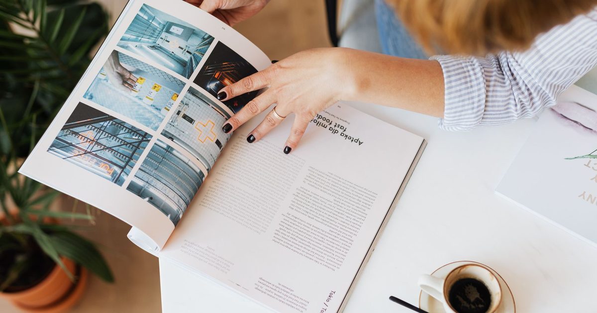 Manos hojeando una revista sobre el escritorio, junto a una taza de café