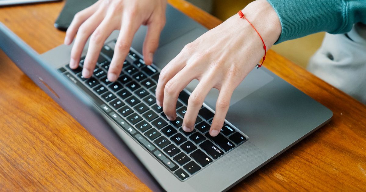 Manos escribiendo en el teclado de un portátil sobre una mesa de madera