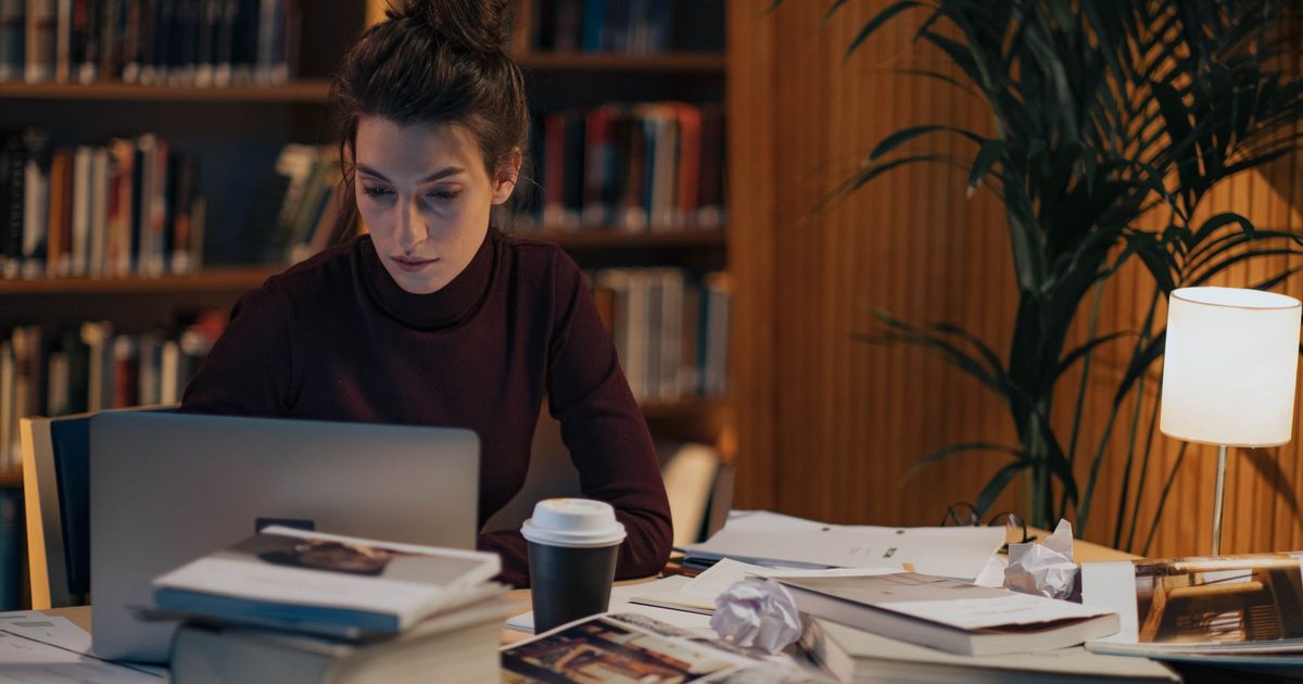 Mujer trabajando en un escritorio cubierto de libros abiertos y un portátil